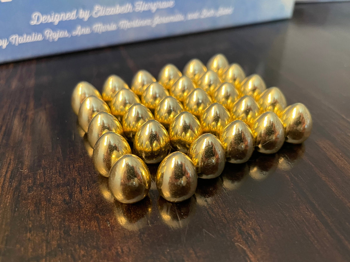 Close-up of about 25 metallic gold egg tokens arranged on a dark wood table, with blurry text in the background