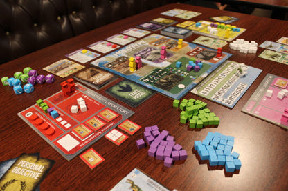 A complex board game, "Holotype," is set up on a wooden table with colorful pieces, dice, cards, and player boards