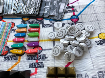 The Tokyo Metro board game shows a grid map with cards, colourful wooden train tokens, and white circular tokens displaying yen and clock symbols
