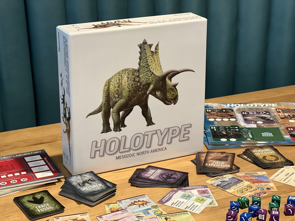 Holotype: Mesozoic North America board game box, with a dinosaur, surrounded by cards, dice, and its board