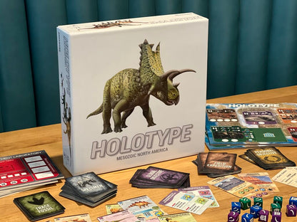 Holotype: Mesozoic North America board game box, with a dinosaur, surrounded by cards, dice, and its board