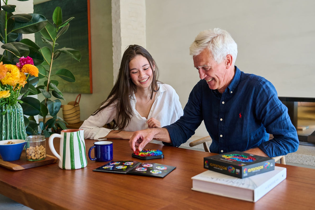 Smiling man and woman playing a colorful IQ Deluxe Pentagon puzzle game together at a wooden table