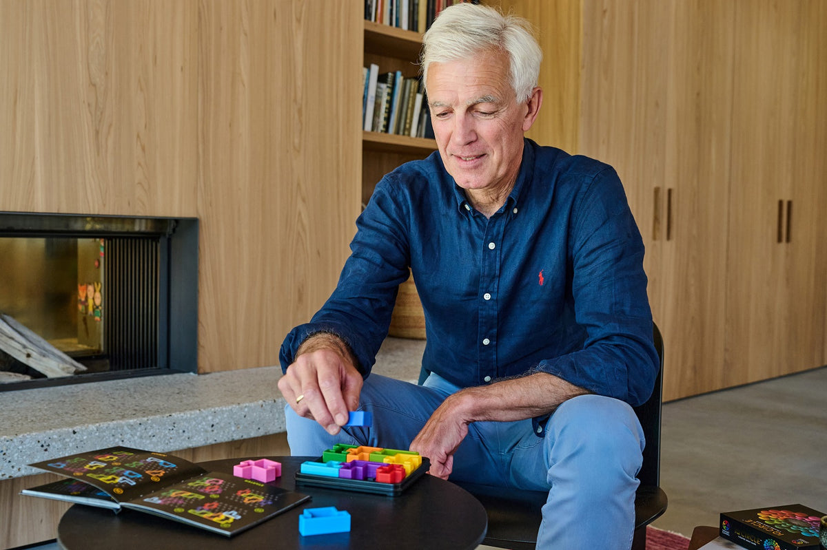 An older man concentrates on placing a blue piece into a colorful IQ Deluxe Square puzzle game