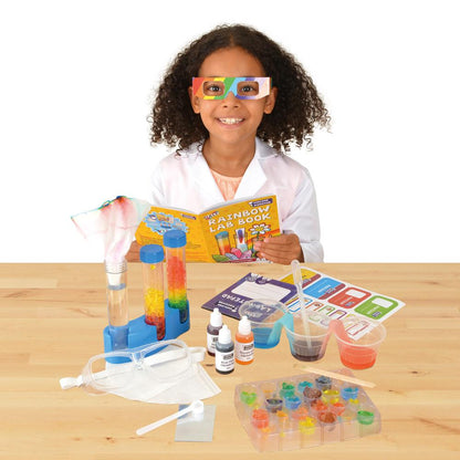Smiling child in a lab coat and rainbow glasses reads a science book, with colourful lab experiments on the table