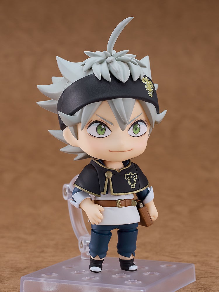 Black Clover's Asta Nendoroid figure stands smiling, he has spiky grey hair, green eyes, and a black outfit with a gold clover
