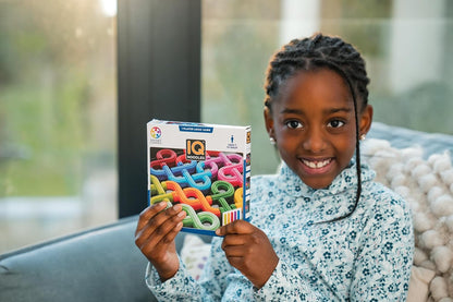 A happy young girl smiles while holding a colorful IQ Noodles logic game box