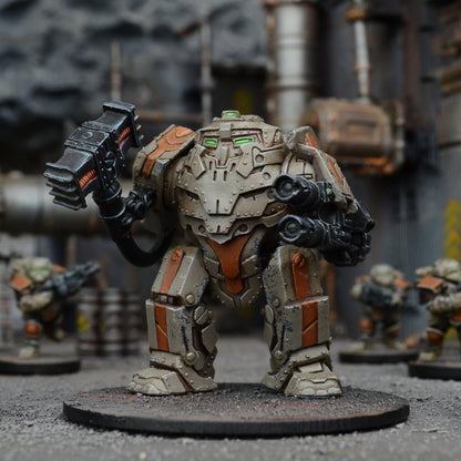 A tabletop miniature of a beige and orange mech with green eyes, wielding a power hammer and arm cannon in an industrial setting.