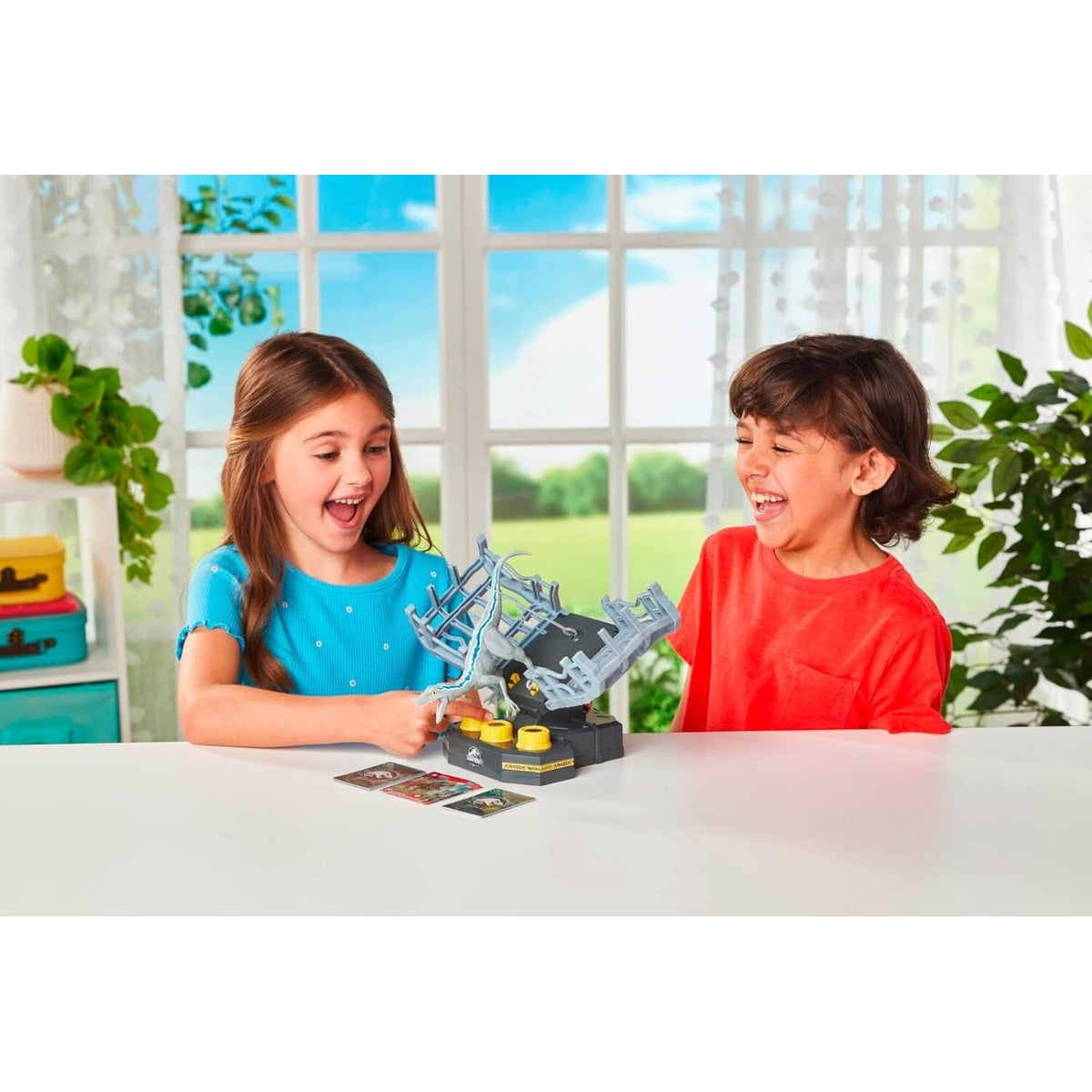 A girl and boy laugh excitedly, playing a Jurassic World dinosaur game with a Velociraptor figure and cards