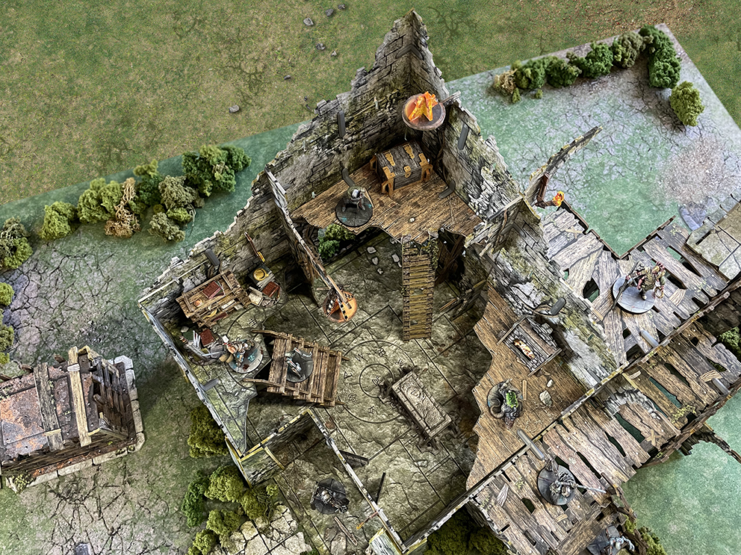 Battle Systems Crypts and Caverns Dungeon Upgrade Pack showcasing detailed ruined stone and wooden terrain pieces for tabletop gaming with miniature figures and vibrant fire effects