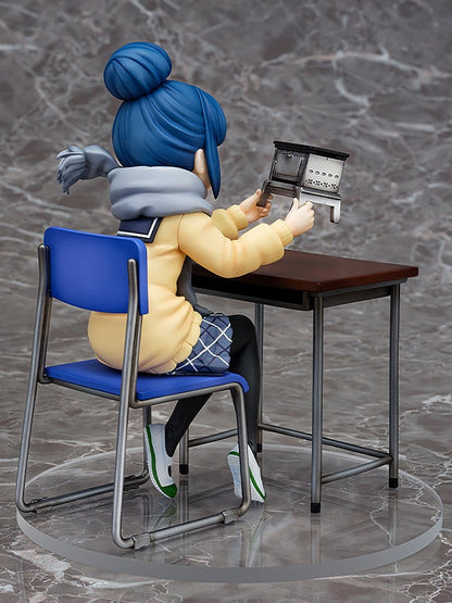 Anime figurine of a blue-haired character in yellow coat and plaid skirt sitting at a desk holding a miniature stove