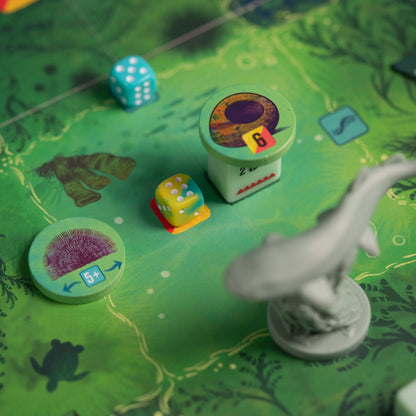 Board game components: Green aquatic map, colourful dice, sea life tokens, and a grey shark miniature