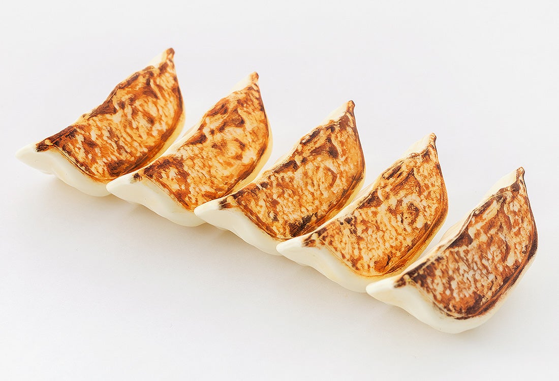 Five golden-brown pan-fried gyoza dumplings lined up in a row