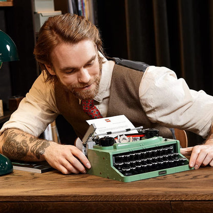 Bearded man leans over a desk, closely inspecting a retro green typewriter
