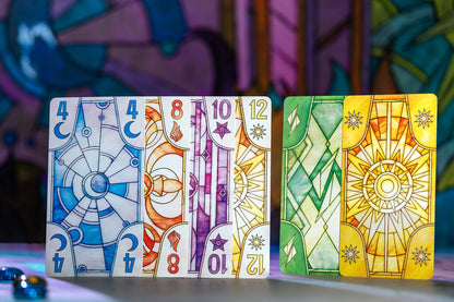 A row of fantasy-themed game cards with stained-glass designs, showing numbered moon, fire, star, and sun elements. Two green/yellow cards on right