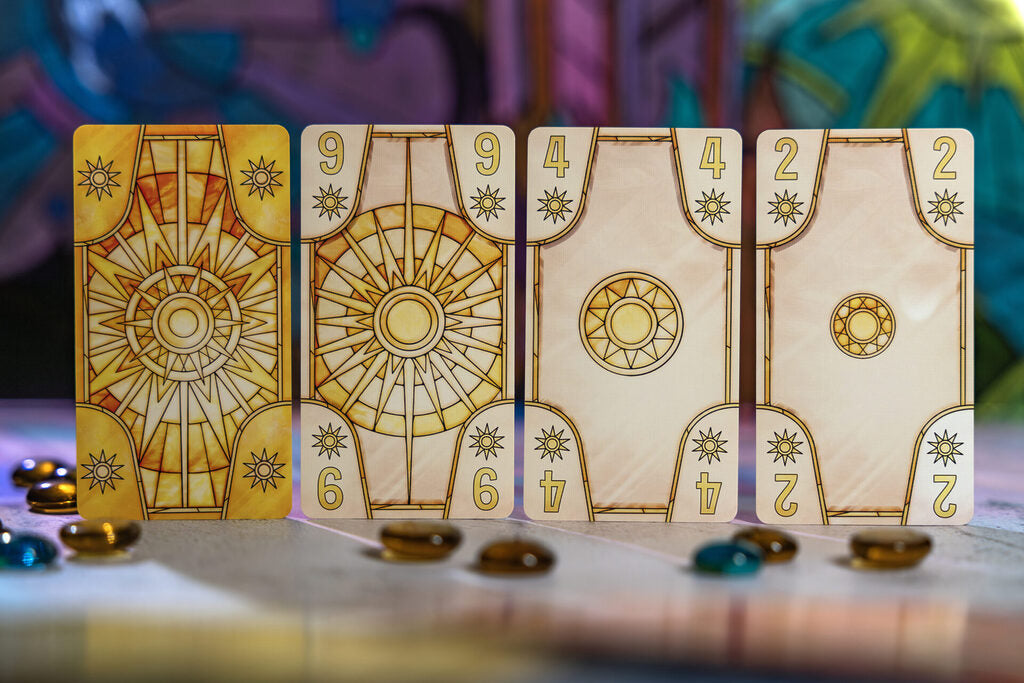 Four sun-themed cards: one face down, three face up with numbers 9, 4, 2. Small colored tokens are scattered nearby