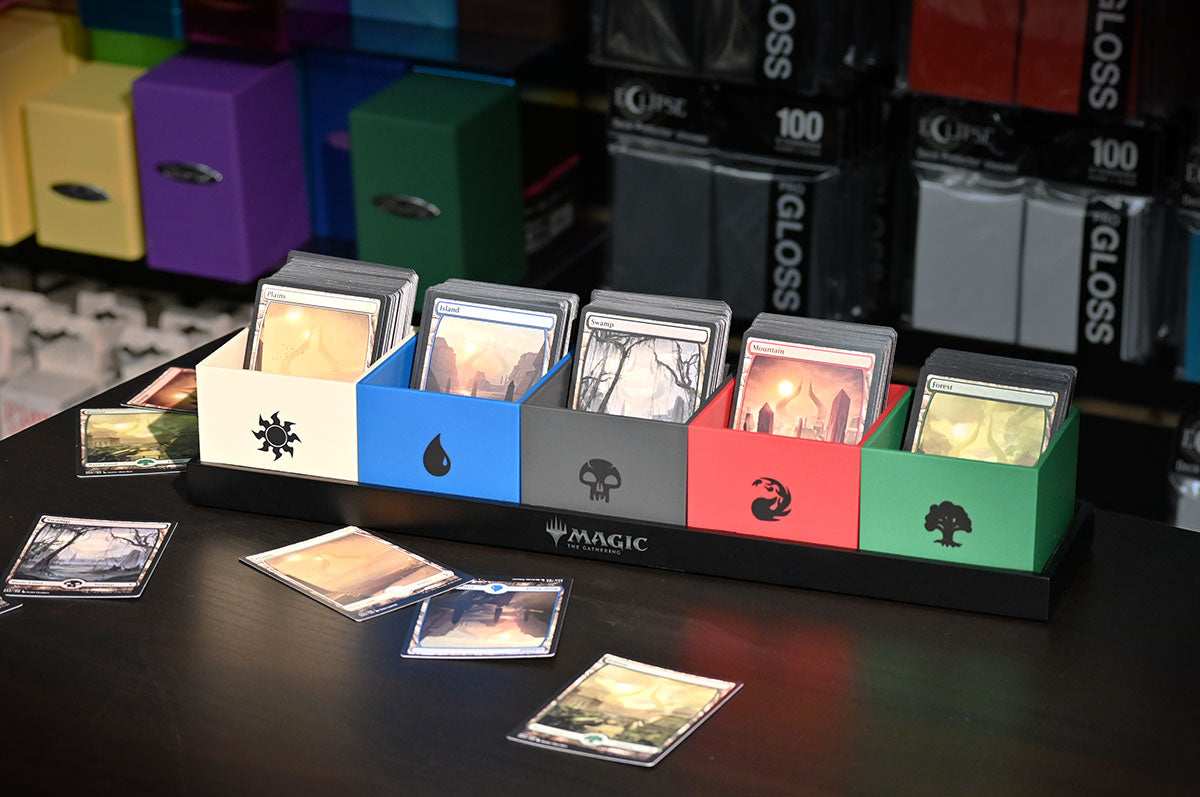 A 5-slot Magic: The Gathering card organizer, colour-coded with mana symbols and filled with cards. Some cards are scattered on the table