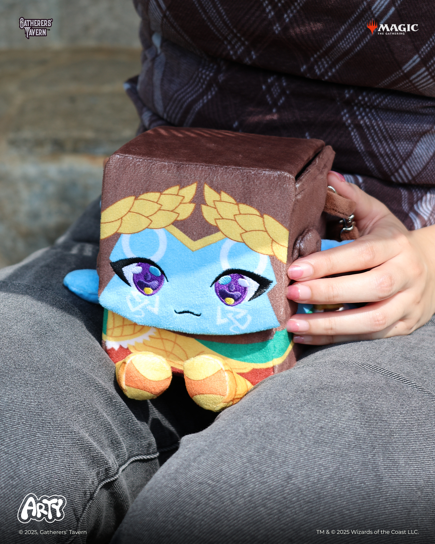 Plush character deck box, featuring blue skin and purple eyes, resting on a person's lap