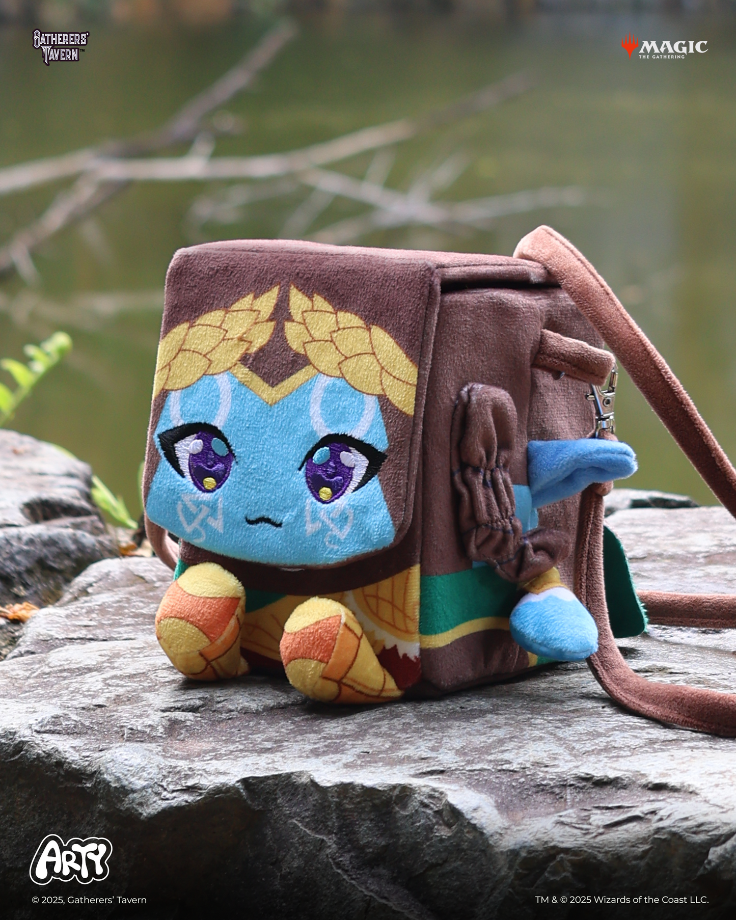 Cube-shaped plush character deck box , styled with a blue face and gold laurels, resting on a rock near water