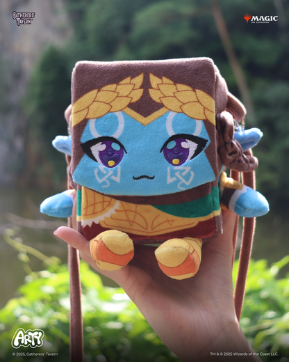 Blocky chibi plush character deck box with a blue face and purple embroidered eyes, held in a hand