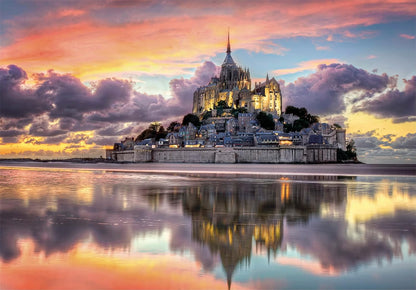 Mont Saint-Michel abbey town illuminated at twilight, reflecting in wet sand under a vibrant orange and pink sky
