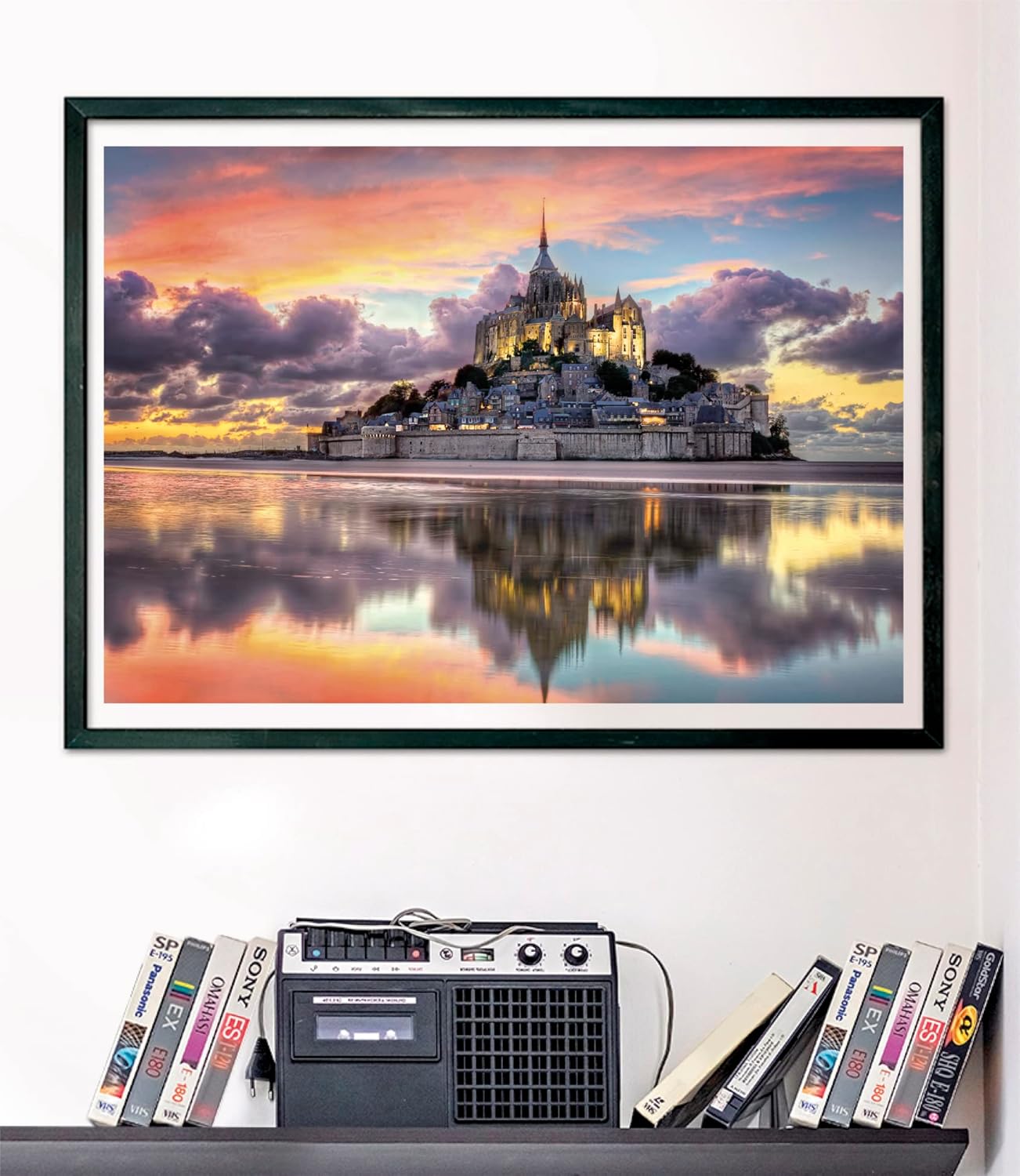 Framed picture of Mont Saint-Michel at sunset, reflected in water. Below it, a boombox and VHS tapes