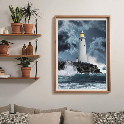 Framed print of a white lighthouse on rocky cliffs, waves crashing under a stormy sky, its lamp brightly lit
