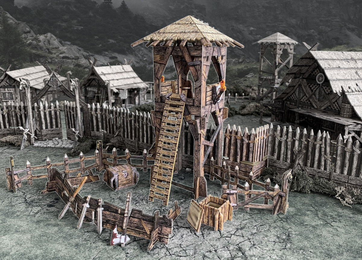Tabletop Viking fortress model: central watchtower, wooden palisades, thatched houses, and scattered weapons.