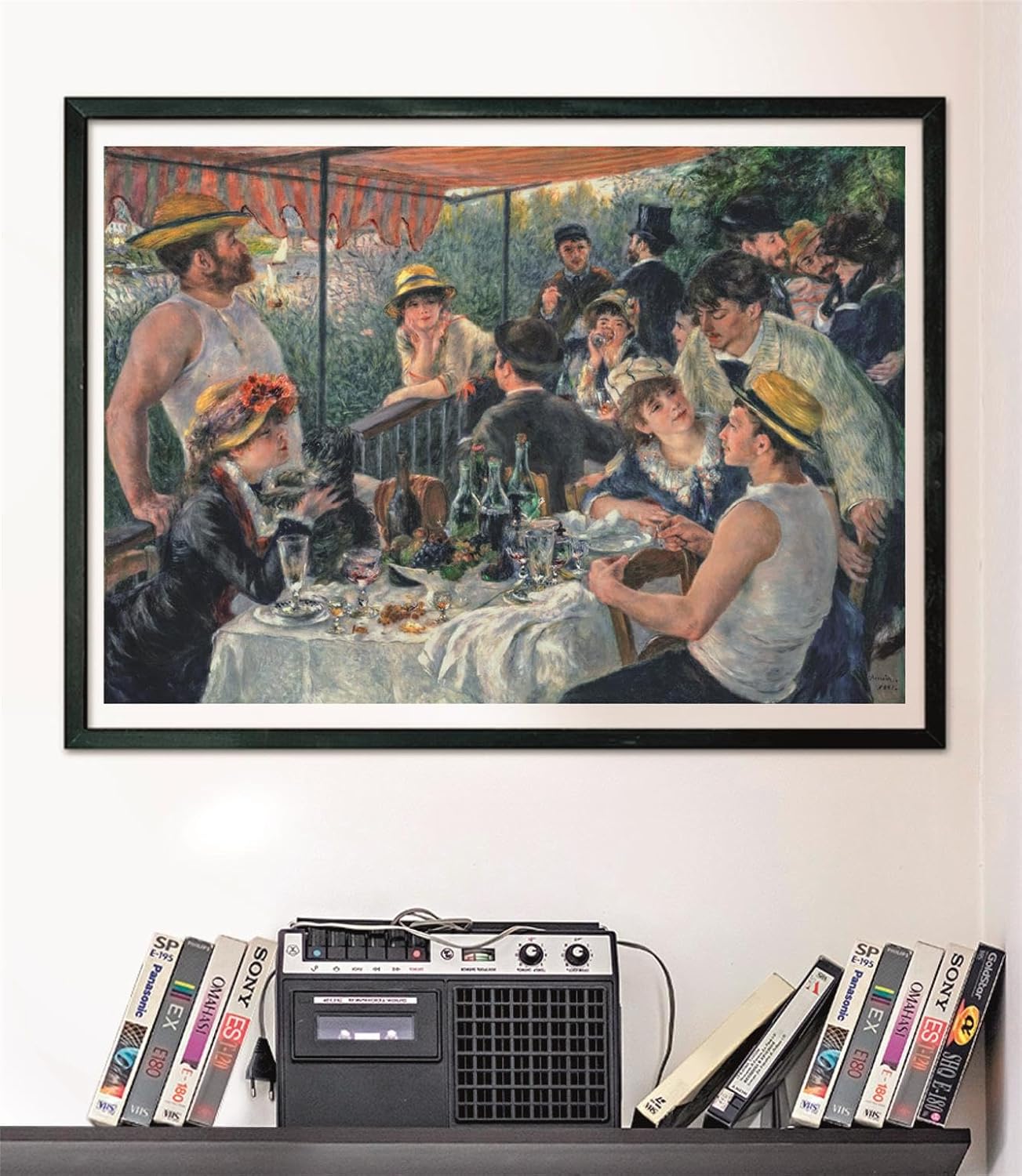 Framed Renoir's "Luncheon of the Boating Party" of people socializing outdoors, above a cassette player and VHS tapes