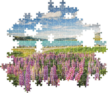 Jigsaw puzzle with missing pieces depicts purple lupins, a blue lake, and snow-capped mountains under a cloudy sky