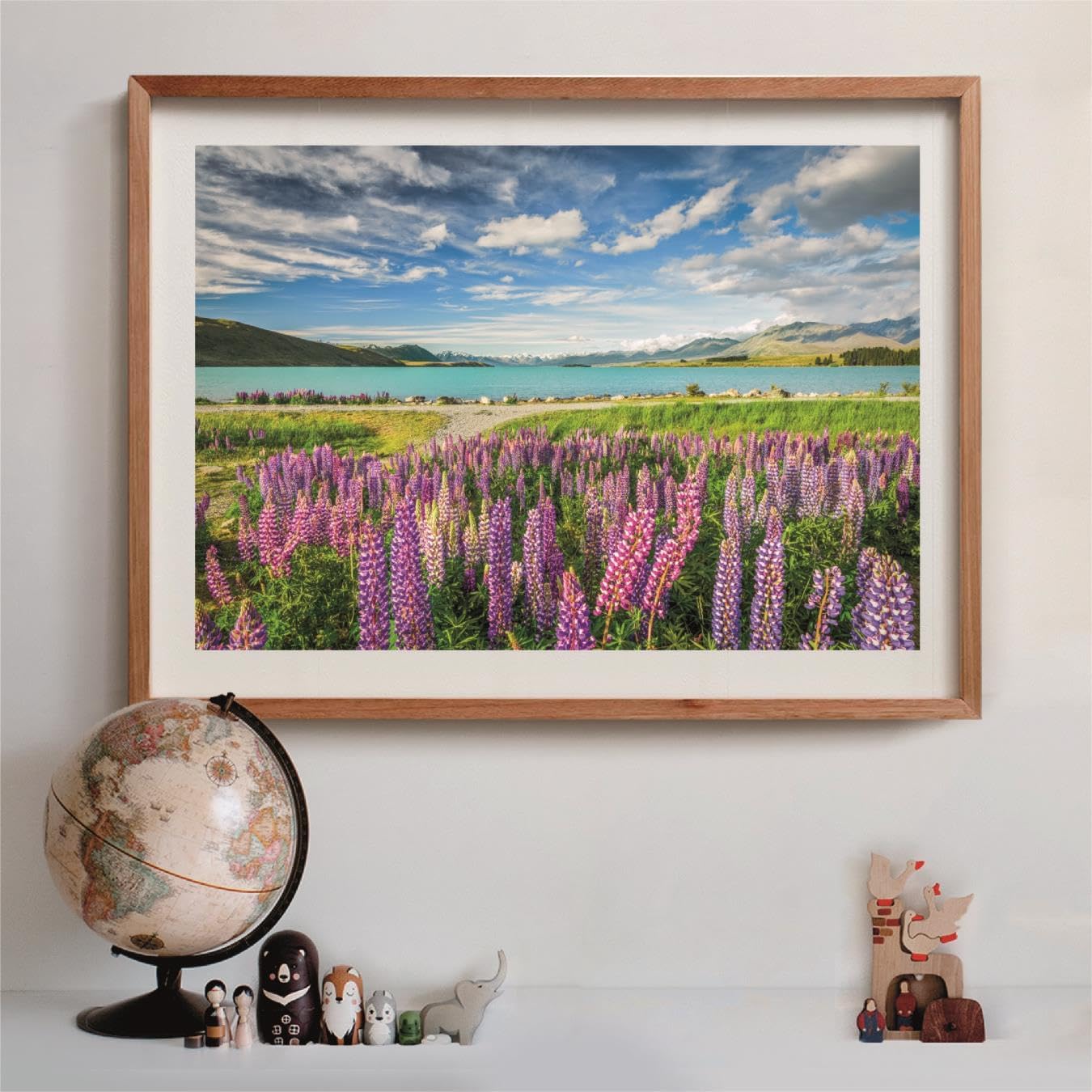 Framed landscape photo: purple lupins, turquoise lake, mountains. A globe and wooden toys sit on a shelf below