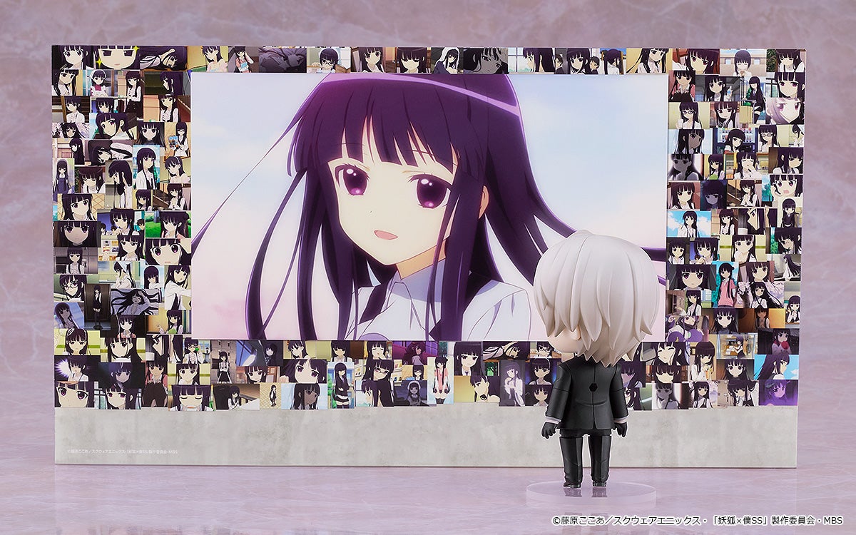 A chibi figure in a black suit looks at a large anime illustration of a dark-haired girl, surrounded by her smaller images.