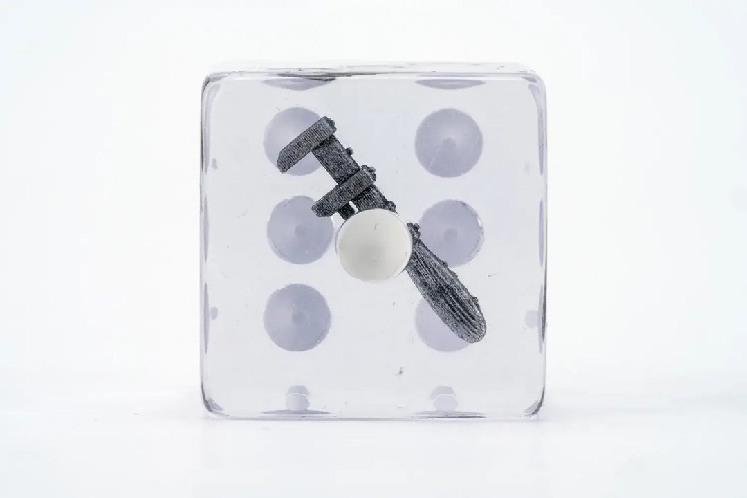 A clear dice contains a small grey caliper measuring a white sphere inside