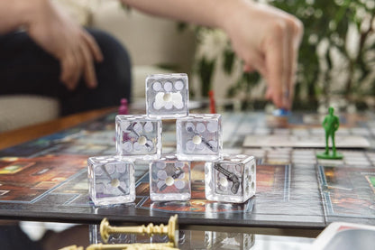 A pyramid of clear dice, containing various miniature Clue game pieces, rests on the game board as a person plays