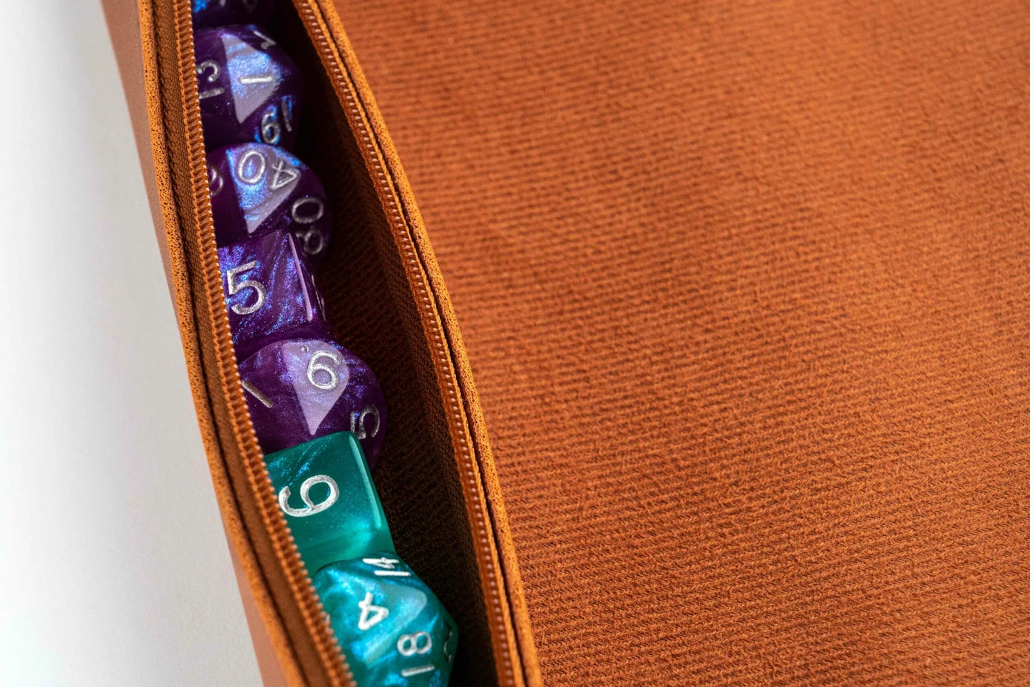 Shiny purple and teal polyhedral dice stored in an open brown zippered pouch