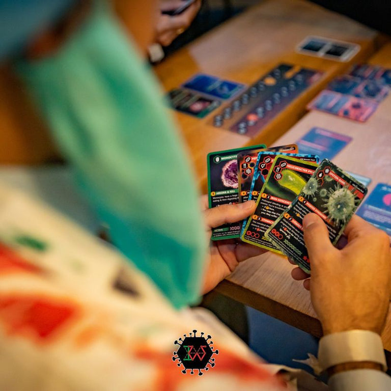 Close-up of hands playing a science-themed card game, holding cards depicting a virus and other biological images