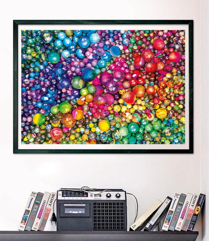 A framed vibrant artwork filled with countless colorful, shiny marbles in a rainbow pattern, displayed above a retro boombox and VHS tapes