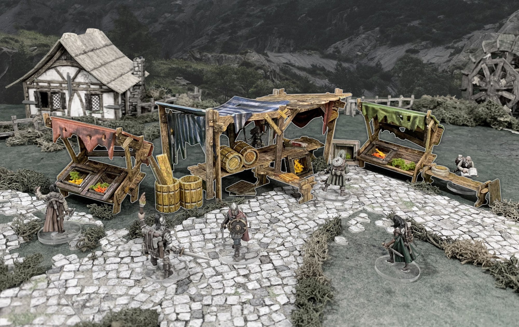 Tabletop fantasy market: Miniatures at three colorful stalls on cobblestones, with a house and water wheel in a village setting.