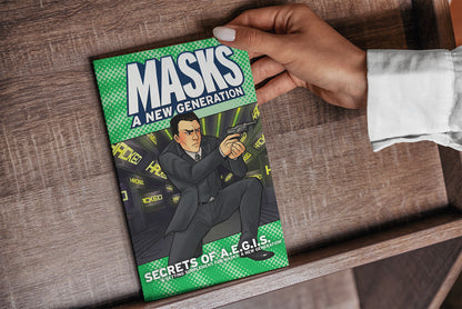Hand holds green 'MASKS A NEW GENERATION' book, showing a man in a suit aiming a pistol.