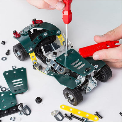 Hands assemble a green Meccano car using a red screwdriver and wrench with parts scattered around