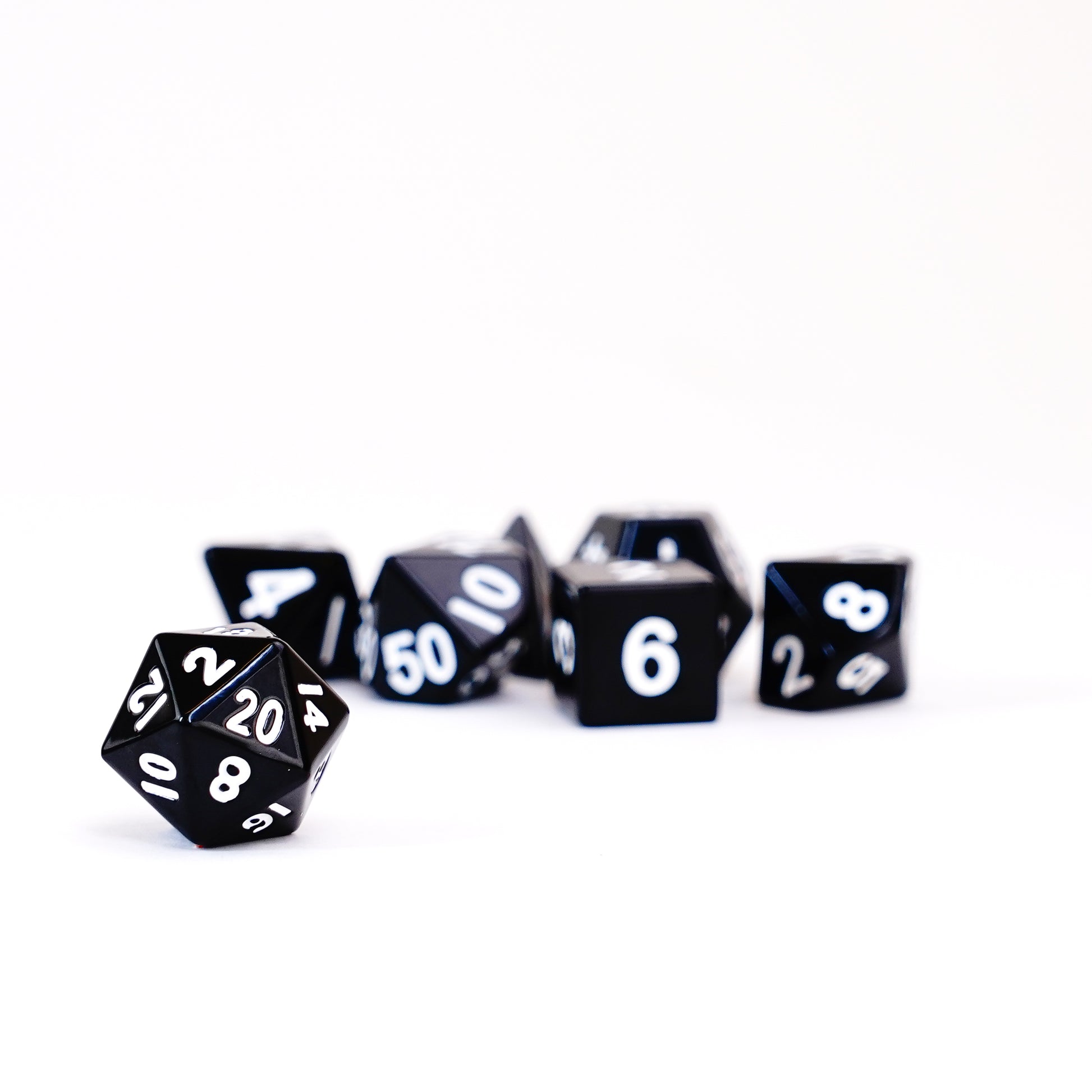 Close-up of black metal D20 die with silver numbers, resting on a black surface
