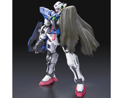 A white, blue, and red Gundam Exia model stands against a dark background, wearing a flowing grey cape and shield