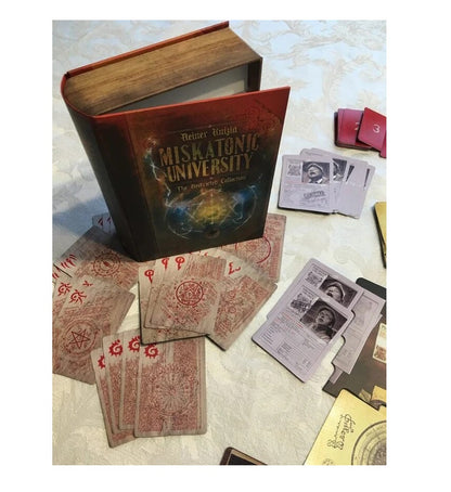 The open, book-shaped box for "Miskatonic University" game is surrounded by various cards with arcane symbols and character portraits.