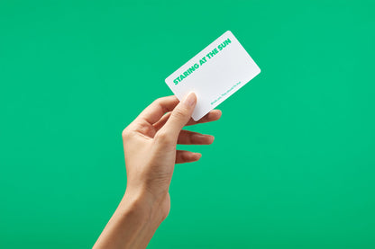 Hand holds card with green text: "STARING AT THE SUN. Blinds you. They should fix that"