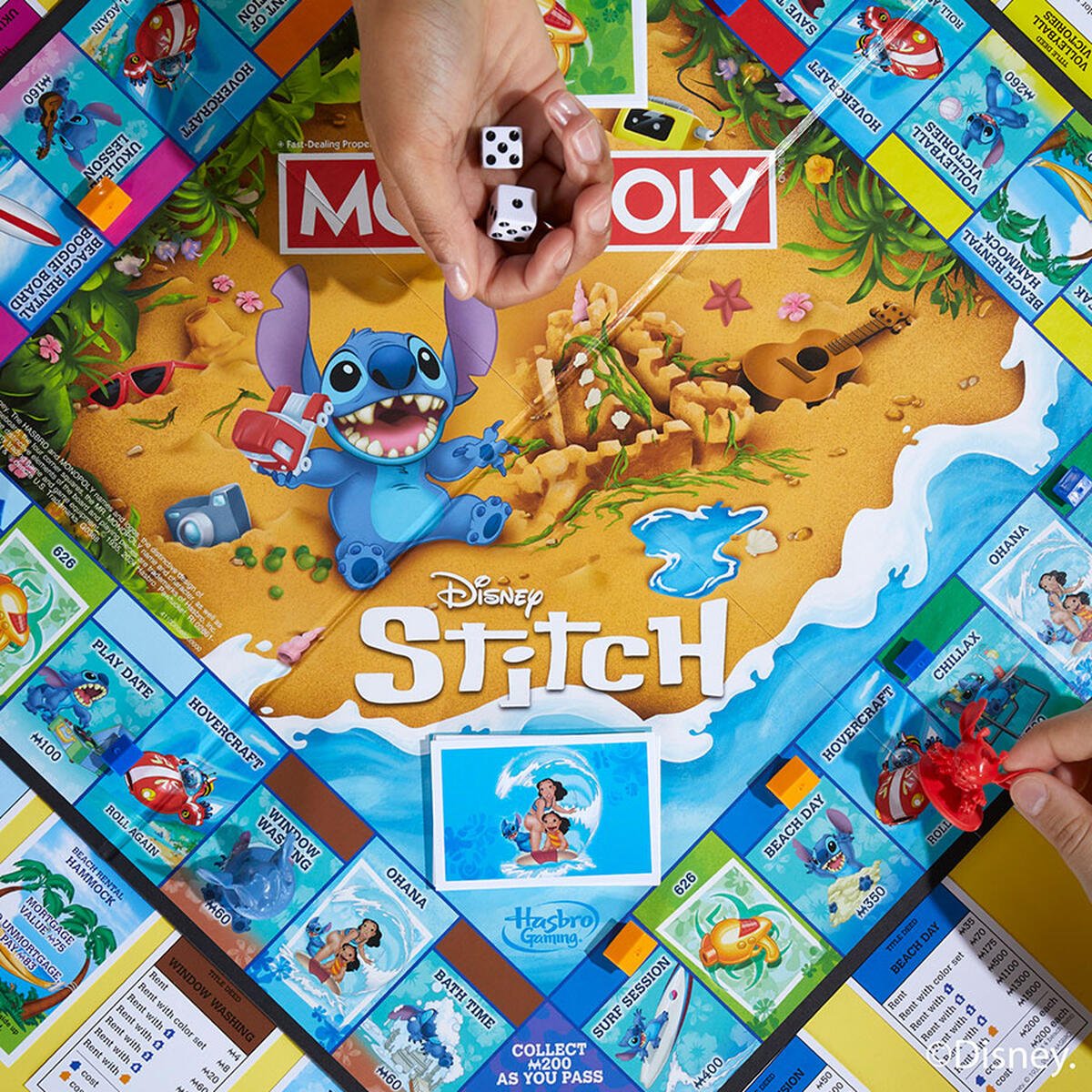 Hand rolls dice on a Disney Stitch Monopoly board featuring Stitch on a beach, as a player moves a red crab piece