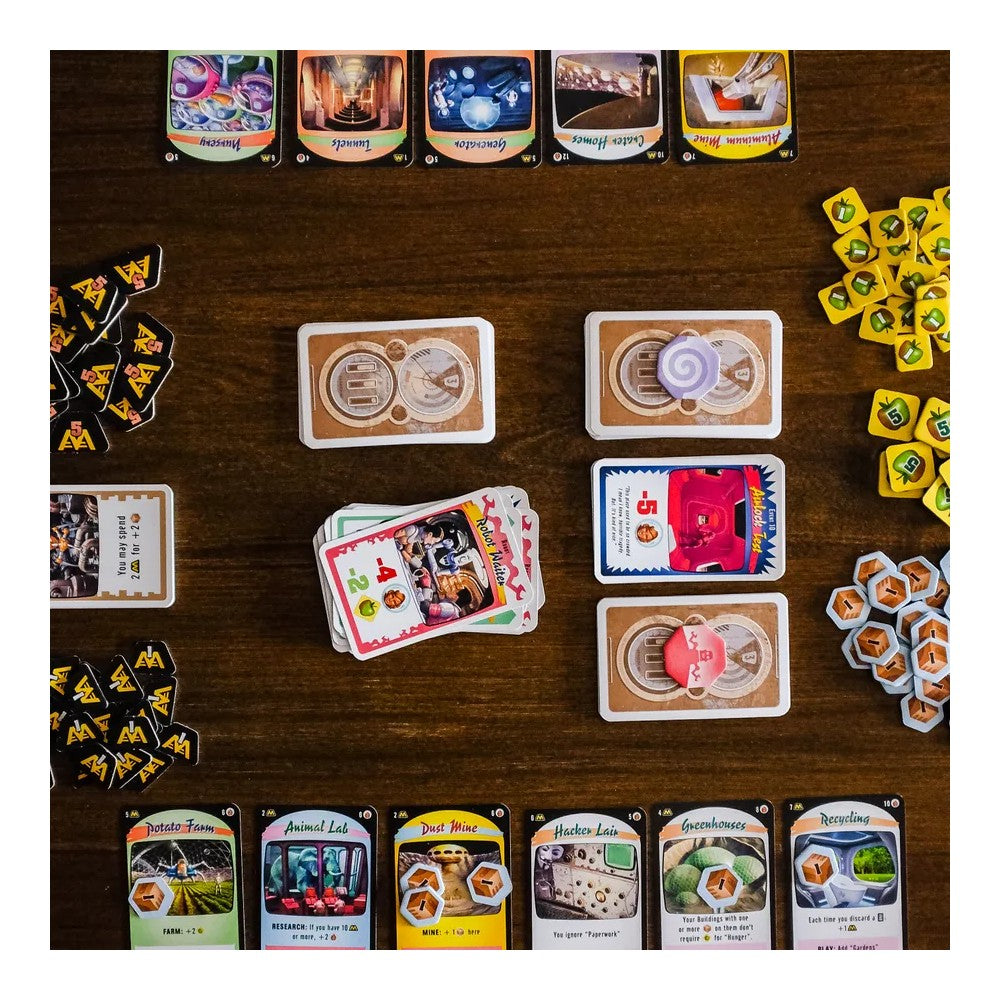 Overhead view of a Moon Colony Bloodbath board game setup with dozens of colorful cards, resource tokens, and stacks on a wood table