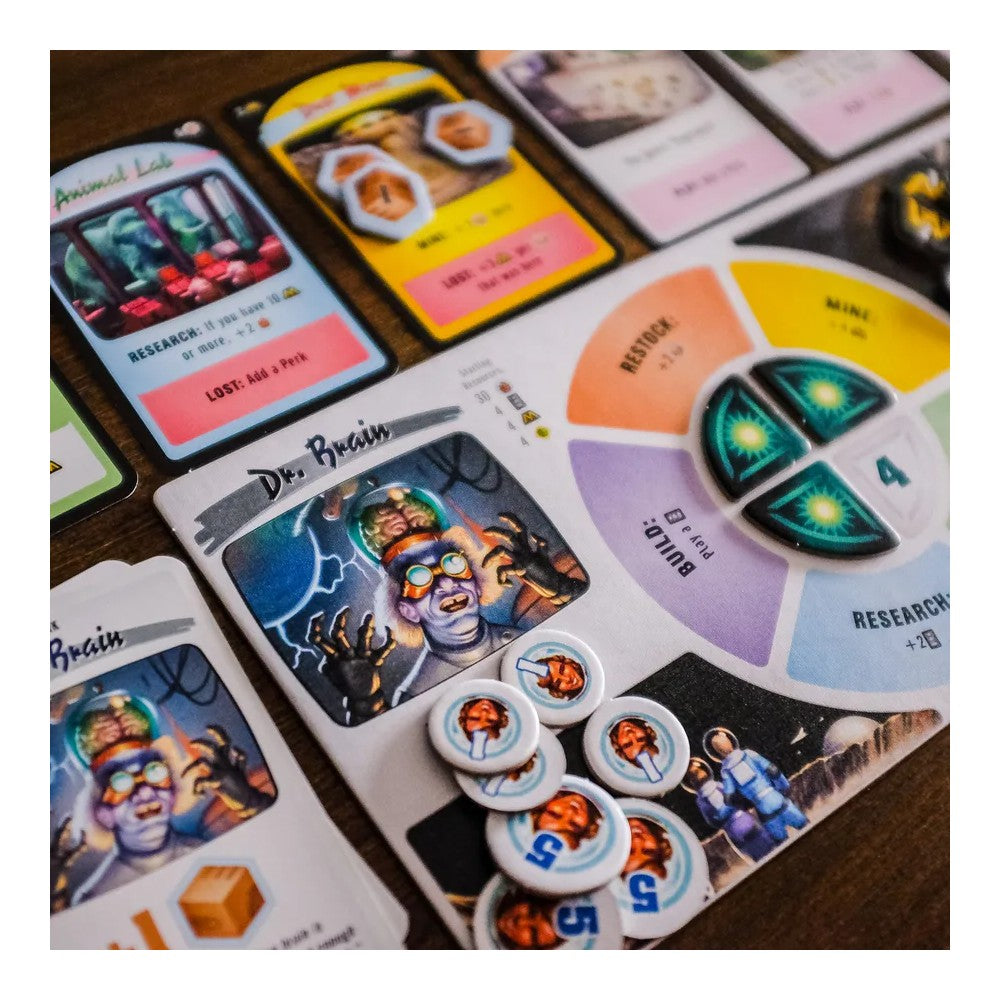 Moon Colony Bloodbath board game components: Dr. Brain character card, brain tokens, resource cards, and a circular action wheel