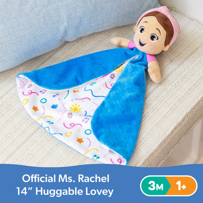 Official Ms. Rachel 14" Huggable Lovey: plush doll with pink headband and smiling face, attached to a blue blanket with a colorful patterned lining, on a textured sofa