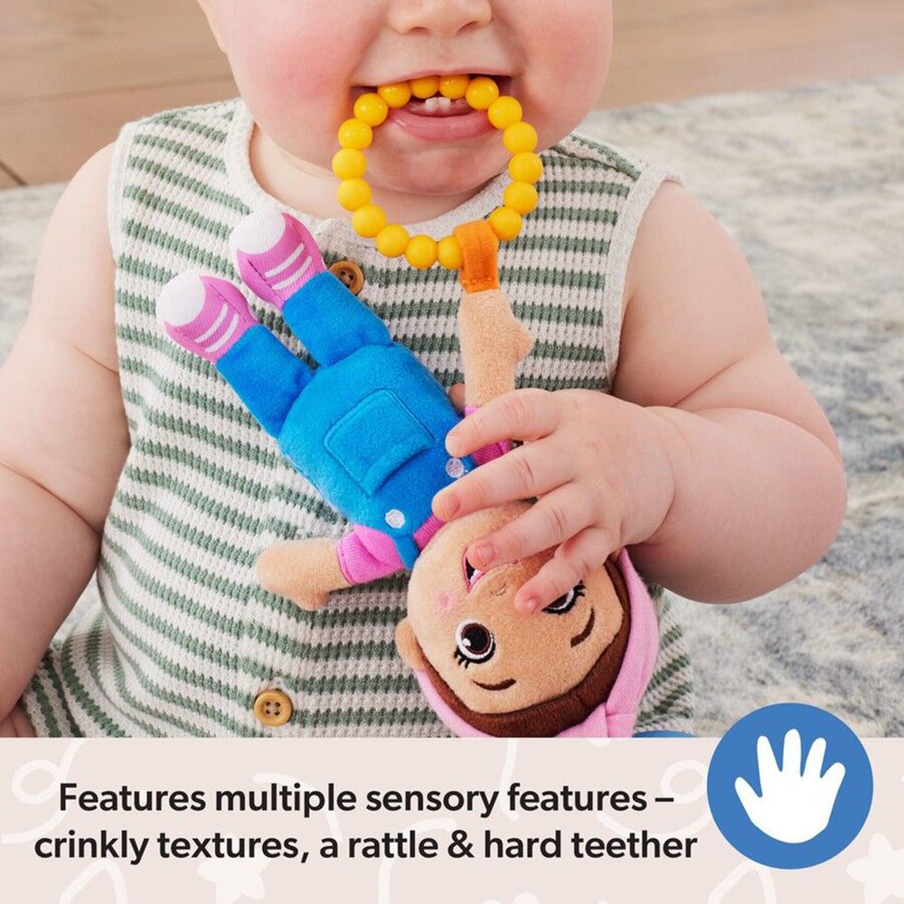 Baby biting a yellow beaded teether and holding a brown-faced doll toy dressed in blue overalls