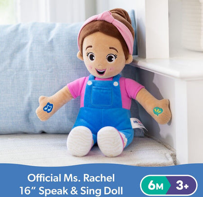 Official Ms. Rachel Speak & Sing plush doll: brown hair, pink headband, pink shirt, blue overalls, and musical note on left arm, sitting on a soft surface
