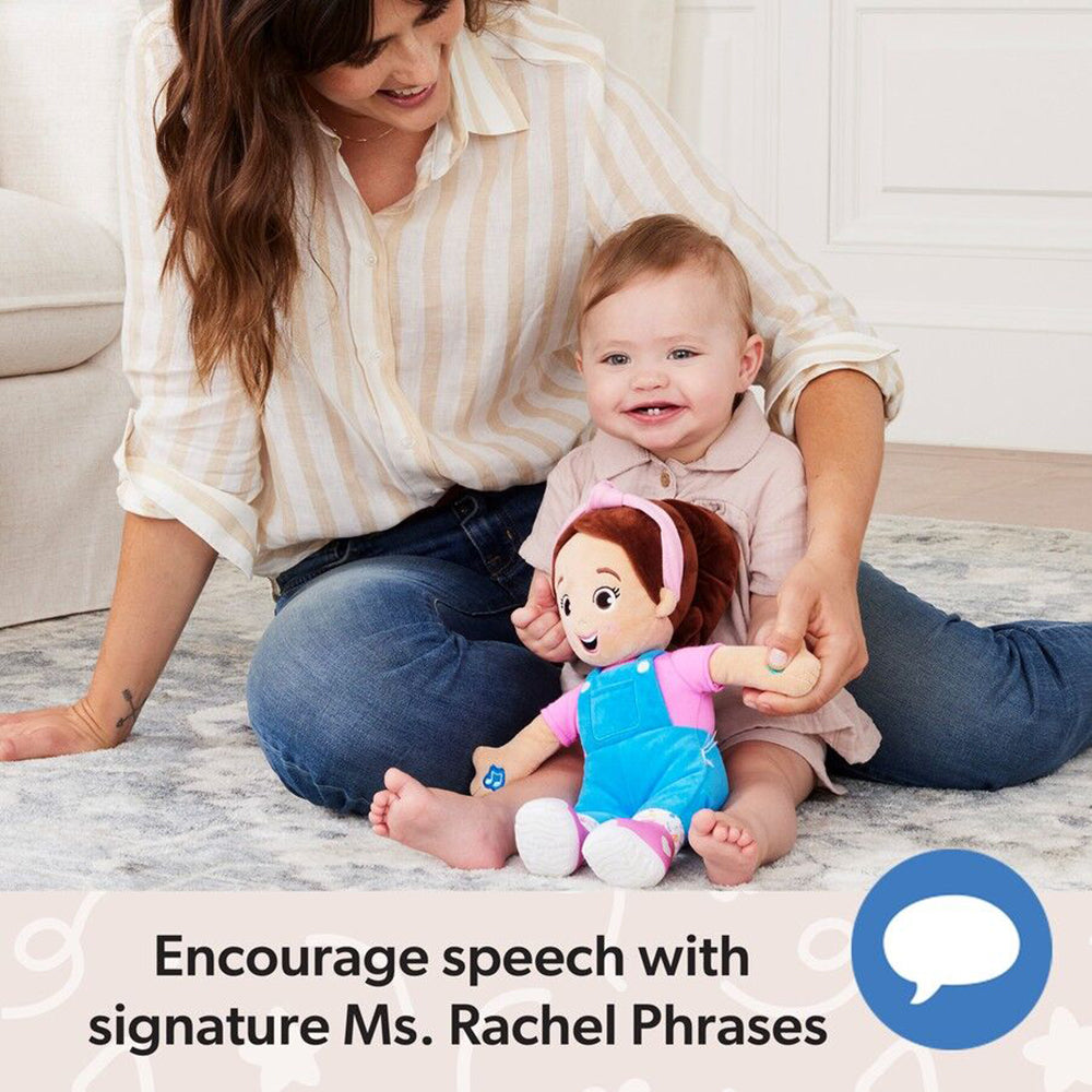 Smiling woman and baby playing on a rug with a Ms. Rachel plush doll wearing blue overalls and a pink shirt